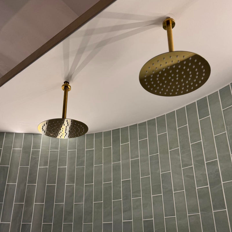 Two gold shower heads mounted on a tiled bathroom wall.