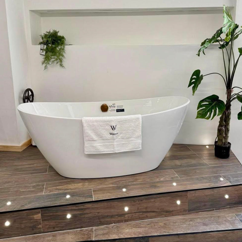 White freestanding bathtub with a towel draped over it in a bathroom setting.